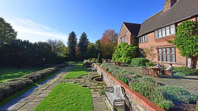 View over a garden with two people sat on a terrace in front of a bricked house